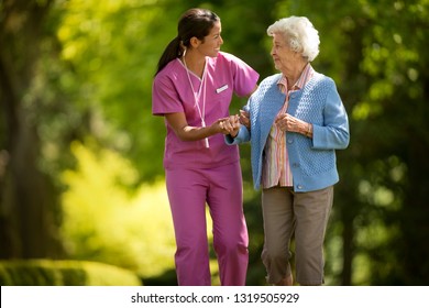 Happy young nurse helpfully assisting an elderly patient to walk outside.