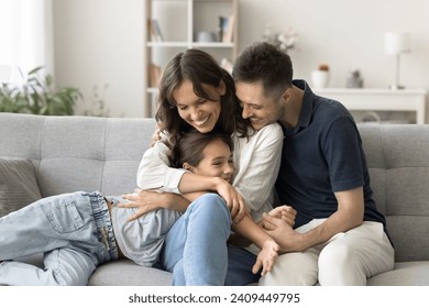 Happy young parents cuddling sweet adorable kid girl on comfortable home couch, hugging child with love, adoration, laughing, spending family leisure with daughter child together - Powered by Shutterstock