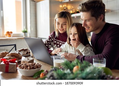 Happy young parents with cute excited small kid daughter using laptop computer at home sitting at Christmas table having virtual party on video call, doing ecommerce family online shopping together. - Powered by Shutterstock