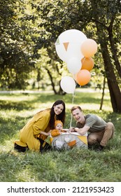 Happy Young Parents Embracing Cute Little Son That Sitting Inside Wicker Basket With Colorful Balloons. Caucasian Family Of Three Celebrating Birthday Party On Fresh Air.