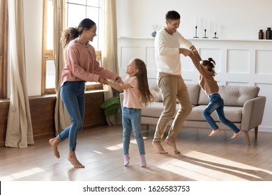 Happy young parents have fun playing with little preschooler excited daughter rest together in living room, smiling family with small kids dancing moving listen to music enjoy weekend at home
