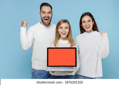 Happy Young Parents Mom Dad With Child Kid Daughter Teen Girl In Sweaters Hold Laptop Computer With Blank Empty Screen Doing Winner Gesture Isolated On Blue Background. Family Day Parenthood Concept