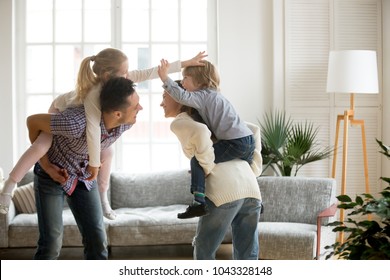 Happy young parents piggybacking son and daughter at home, smiling father and mother holding little kids on back spending time together, family having fun enjoying activity playing with children - Shutterstock ID 1043328148