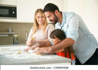 Happy Young Parents Teaching Daughter To Roll Dough On Kitchen Desk With Flour Messy. Young Couple And Their Girl Baking Buns Or Pies Together. Family Cooking Concept