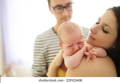 Happy Young Parents With Their Crying Newborn Baby Girl At Home