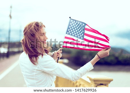 Happy young patriot urban woman with toothy smile stretching USA flag, profile view