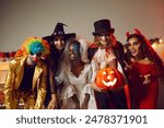 Happy young people dressed up as different spooky characters, with scary makeup on faces having fun at Halloween costume party. Group portrait of adult friends with traditional smiley jack-o-lantern