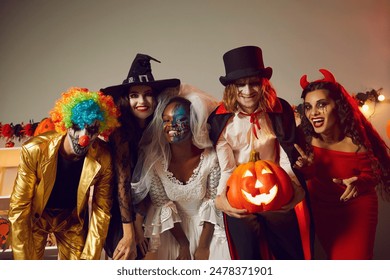 Happy young people dressed up as different spooky characters, with scary makeup on faces having fun at Halloween costume party. Group portrait of adult friends with traditional smiley jack-o-lantern - Powered by Shutterstock