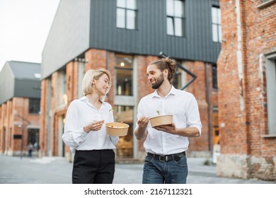 Happy young people eating healthy salad for lunch. Cheerful business parnners having a break on walking on city street and snacking on a vegan takeaway meal of green veggies laughing together. - Powered by Shutterstock