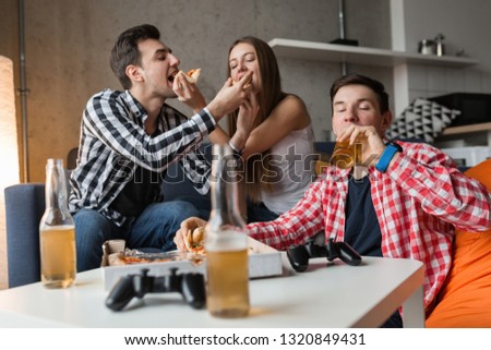 happy young people eating pizza, drinking beer, having fun, friends party at home, hipster company together, two men one woman, smiling, positive, relaxed, hang out, laughing, funny emotions