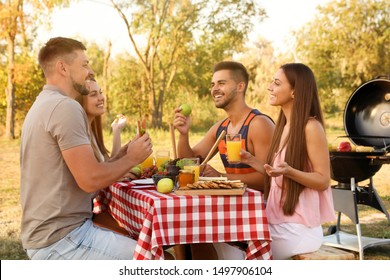 Happy young people having picnic at table in park - Powered by Shutterstock