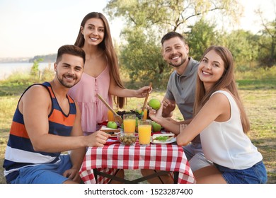 Happy young people having picnic at table in park - Powered by Shutterstock