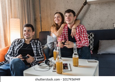 happy young people playing video games, having fun, friends party at home, hipster company together, two men one woman, smiling, positive, relaxed, laughing, beer bottles on table