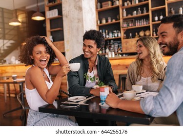 Jóvenes felices sentados alrededor de una mesa de café y tomando café. Grupo multirracial de amigos disfrutando del café juntos en un restaurante.