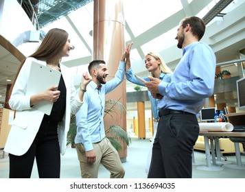 Happy young people standing in office and giving high five to their colleagues.