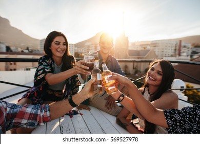 Happy Young People Toasting Drinks At A Rooftop Party. Young Friends Hanging Out And Enjoying Drinks.