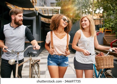 Happy young people walking down the city street with their bicycles and smiling. Young man and women on road with their bikes.