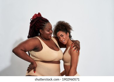Happy young plump african american woman hugging with slim girl posing in lingerie on light background. Body positive concept