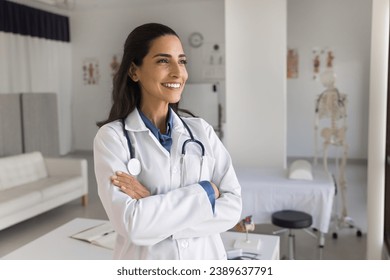 Happy young practitioner doctor posing in medical office, standing with hands crossed, looking away, smiling, thinking on successful therapy for patients, enjoying occupation - Powered by Shutterstock