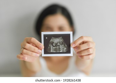 Happy Young Pregnant woman holding showing ultrasound scan photo. Smiling Asian Mother with sonogram of her unborn baby. Concept of pregnancy, Maternity prenatal care