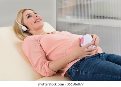 Happy Young Pregnant Woman Listening To Heart Beat Through Headphones On Bed At Home