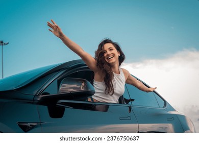 Happy young pretty woman holding hands to the side and leaning out of car side view window. Travel adventure drive, happy summer vacation concept - Powered by Shutterstock