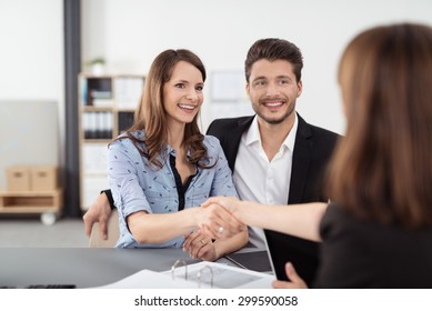 Happy Young Professional Couple Shaking Hands with a Real Estate Agent After Some Business Discussions Inside the Office.