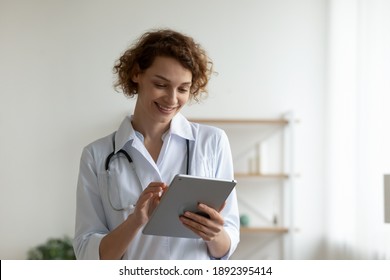 Happy Young Professional General Practitioner In White Medical Uniform Involved In Communicating Distantly With Patient Using Digital Computer Tablet At Clinic, Modern Technology And Medicare Concept.