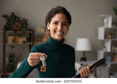 Happy young professional hispanic latin female realtor or broker holding keys and paper agreements in hands, proposing renovated news stylish apartment to client, real estate service concept.