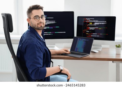 Happy young programmer working with laptop in office