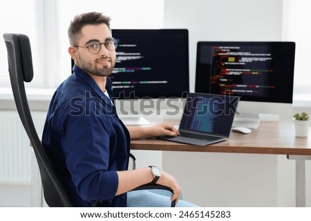 Happy young programmer working with laptop in office