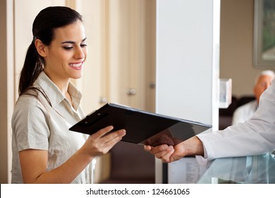 Happy young receptionist taking clipboard from doctor while standing at reception - Powered by Shutterstock