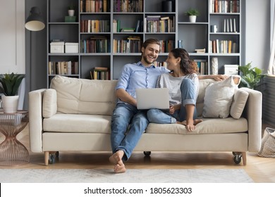 Happy Young Relaxed Couple Sitting On Sofa With Laptop On Laps, Discussing Funny Movie, Enjoying Watching Comedian Film, Shopping Online Or Web Surfing, Full Length Front View, Leisure Pastime Concept