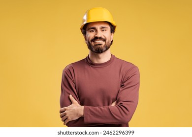 Happy young repairman wearing helmet standing crossed arms looking at camera, isolated on yellow. Work protection, construction safety concept - Powered by Shutterstock