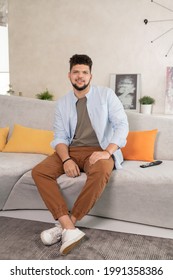 Happy young restful man sitting on couch in home environment