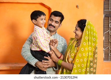 Happy Young Rural Indian Family Laughing. Father Holding Little Child Boy And Mother Wearing Sari Smiling,Couple Wearing Traditional Cloths With Kid.