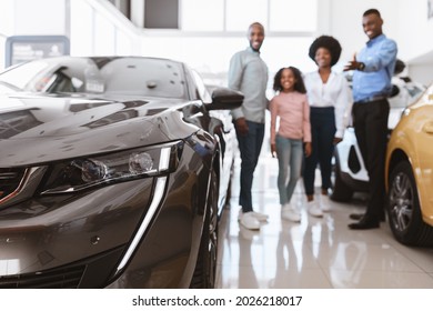 Happy Young Salesman Helping African American Family Choose Luxury Car At Vehicle Dealership, Selective Focus. Black Parents With Kid Consulting Manager About New Auto, Copy Space