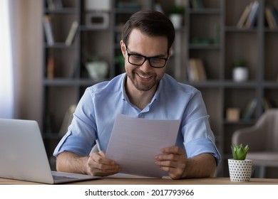 Happy Young Self Employed Businessman Enjoy Reading Good News In Letter Receive Official Paper About Tax Refund Credit Loan Approval. Smiling Young Male Freelancer In Glasses Study Financial Report