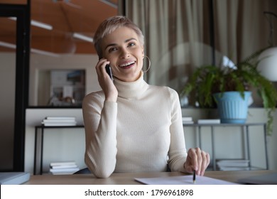 Happy young short haired female employee calling friends, chatting in office distracted from job. Smiling young businesswoman holding negotiations mobile phone call, discussing project with client.