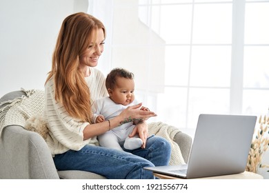 Happy young single caucasian mother holding cute small african mixed race infant baby girl, child daughter looking at laptop computer working from home, video calling, having remote virtual meeting. - Powered by Shutterstock