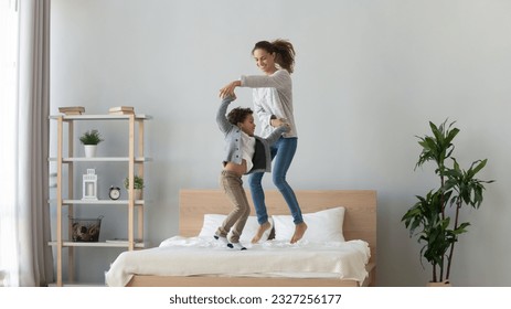 Happy young single mommy jumping, twisting, dancing with cute small smiling son on bed. Overjoyed excited family of two having fun together, spending active weekend leisure time at home. - Powered by Shutterstock