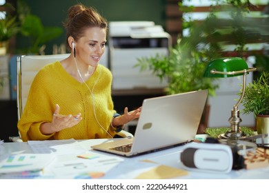 Happy Young Small Business Owner Woman In Yellow Sweater With Laptop Video Chatting In The Modern Green Office.