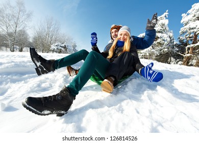 Happy Young Smiling Adult People In Warm Clothing Sledding On Snow At Winter Outdoors