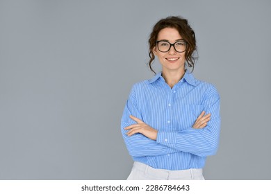 Happy young smiling confident professional business woman wearing blue shirt and glasses, happy pretty female executive looking at camera, standing arms crossed isolated at gray background, portrait. - Powered by Shutterstock