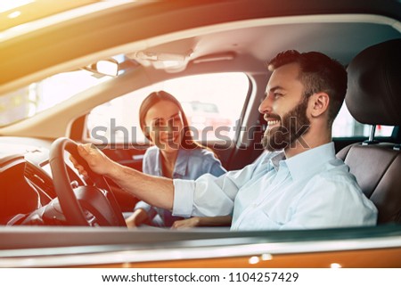 Happy young smiling couple riding in car on the road. Handsome bearded man is sitting at the wheel.