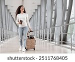 Happy Young Smiling Woman Walking With Luggage At Airport Terminal, Cheerful Middle Eastern Female Holding Passport With Tickets And Carrying Suitcase While Going To Flight Departure Gate, Copy Space