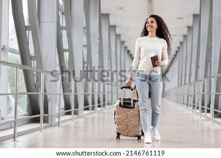 Happy Young Smiling Woman Walking With Luggage At Airport Terminal, Cheerful Middle Eastern Female Holding Passport With Tickets And Carrying Suitcase While Going To Flight Departure Gate, Copy Space