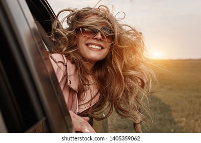 Happy young smilling woman enjoying nature traveling in a car and looking out.