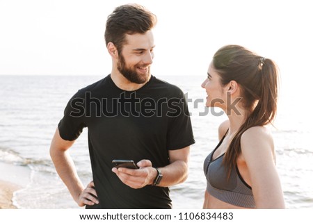 Happy young sport couple talking while standing at the beach with mobile phone