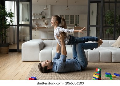 Happy young strong father lifting in air cute small kid daughter, lying on floor carpet in modern living room, playing airplane, imagining travelling or having fun practicing acro yoga exercises. - Powered by Shutterstock